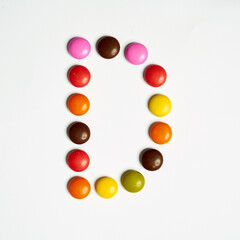 Colored chocolate coated candy alphabet on white background. D