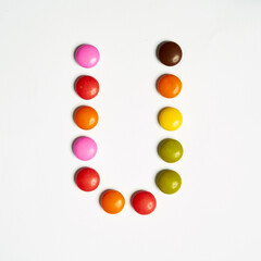 Colored chocolate coated candy alphabet on white background. U