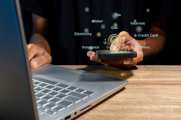 Man using a laptop and holding a smartphone to calculate the monthly bills or household expenses