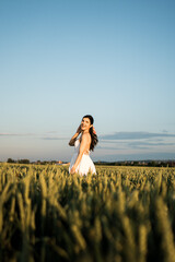 Beautiful woman in a white dress posing and dancing in a green wheat field. Freedom concept.Photo session in a green wheat field