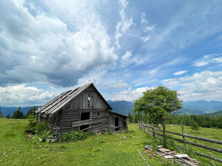 Woodel old hut against green mountains and dramatic sky.