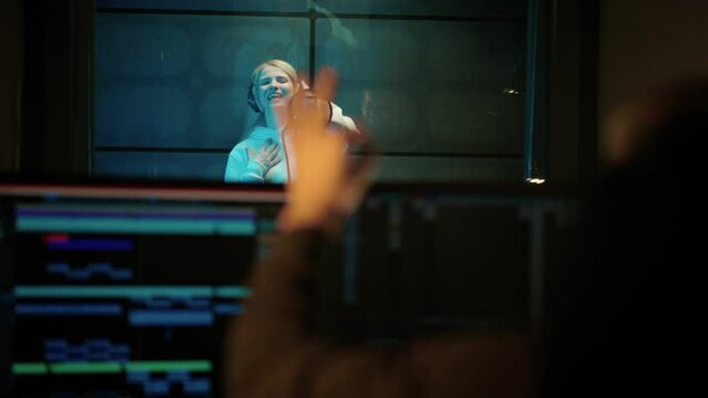 Male studio engineer showing OK symbol to woman singer in recording studio. Professional musicians working together in modern record label, creating new single for music album, talented people team