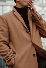Young man smoking in the city, fashion details of beige brown men's coat and black turtleneck....