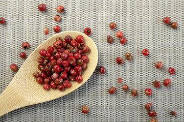 Red or pink peppercorns on wooden spoon on grey textured cutting board background