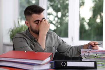 Naklejka premium Overwhelmed man sitting at table with documents in office