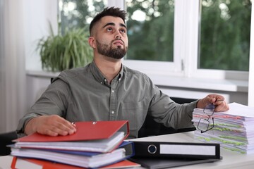 Naklejka premium Overwhelmed man sitting at table with documents in office