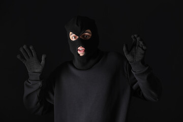 Thief in hoodie raising hands against black background