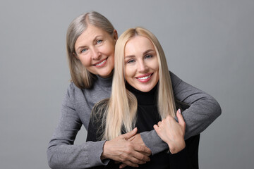 Family portrait of young woman and her mother on grey background