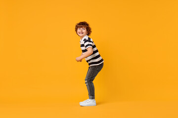 Fototapeta premium Happy little boy dancing on yellow background. Space for text