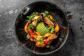 Vibrant gourmet salad with grilled chicken, avocado slices, cherry tomatoes, and greens on a dark plate against a dark background