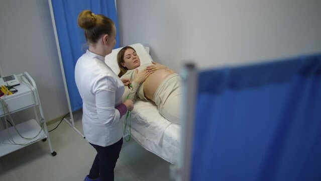 Slow motion. A female doctor measures the standing height of the uterine fundus in a pregnant woman with a measuring tape, who is lying on her back on an examination couch in the doctor's office