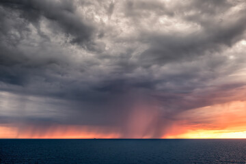 A large dramatic storm and falling rain as the sun sets over the Mediterranean sea off the coast of Marseille