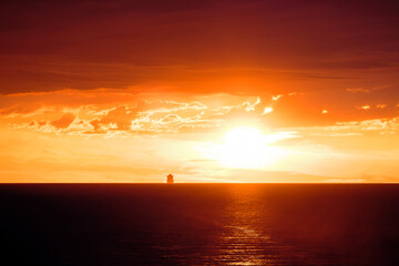 A large ship silhouetted on the horizon of the Mediterranean sea against a dramatic orange sunset