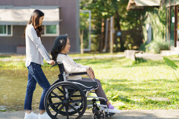 Asian senior woman in wheelchair with happy daughter. Family relationship retired woman sitting on wheelchair in the park age care at retirement home.