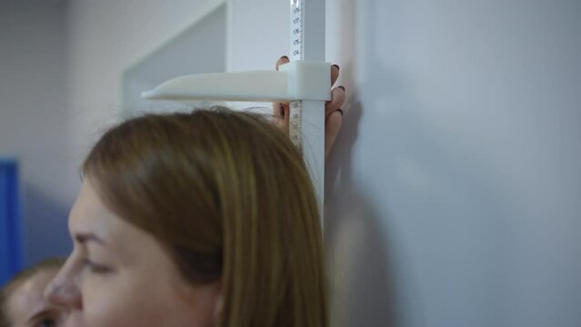 Slow motion. Close-up. The female doctor moves the stadiometer bar down until it touches the head of the female patient. A doctor measures a patient's height in his office during a medical examination