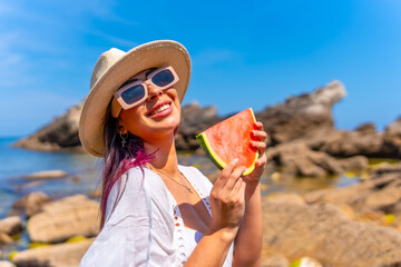 A woman is holding a watermelon slice in her hand while wearing a straw hat