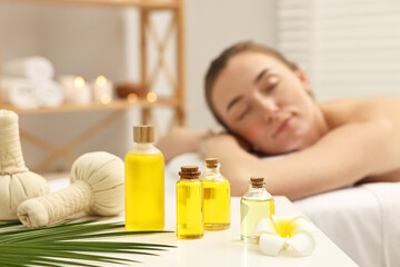 Aromatherapy. Woman relaxing on massage couch in spa salon, focus on bottles of essential oils, herbal bags and plumeria flower