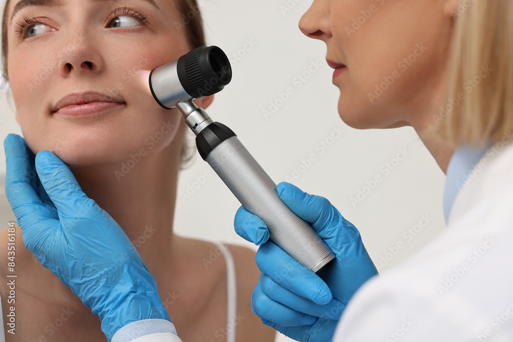 Poster Dermatologist with dermatoscope examining patient`s face in clinic, closeup