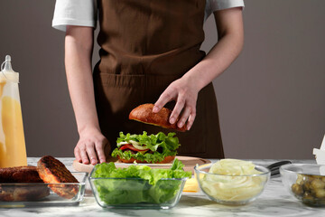 Woman making delicious vegetarian burger at white marble table, closeup