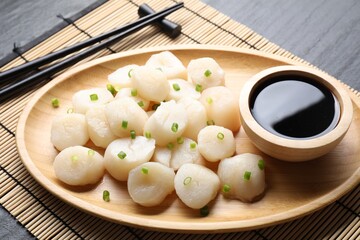 Raw scallops with green onion and soy sauce on dark table, closeup