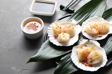 Raw scallops with spices, lemon zest, shells and sauces on grey textured table, closeup