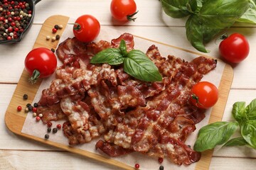 Slices of tasty fried bacon with different spices and tomatoes on wooden table, flat lay