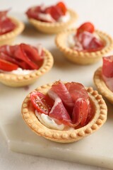 Delicious canapes with jamon, cream cheese and cherry tomatoes on light table, closeup