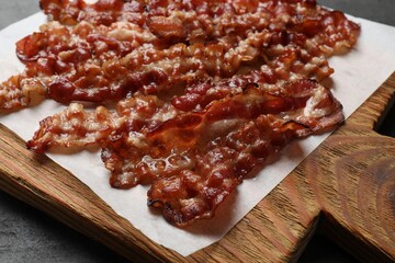 Slices of tasty fried bacon on black table, closeup