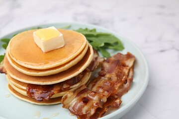 Tasty pancakes with butter, fried bacon and fresh arugula on white marble table, closeup