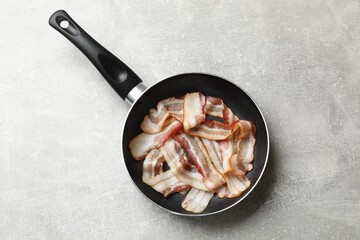 Delicious bacon slices in frying pan on light grey table, top view