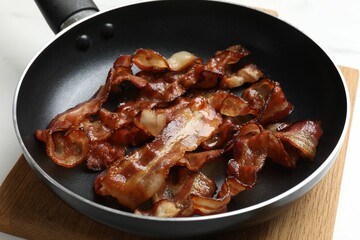 Delicious bacon slices in frying pan on white table, closeup