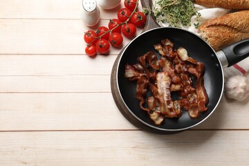 Delicious bacon slices in frying pan and products on light wooden table, flat lay. Space for text
