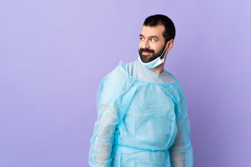 Surgeon man with beard with blue uniform over isolated purple background . Portrait