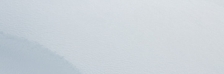 Beautiful winter background with snowy ground. Natural snow texture. Wind sculpted patterns on snow surface. Wide panoramic texture for background and design. Closeup top view with copy space.