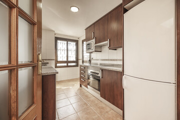 A kitchen with brown wooden furniture, with integrated appliances, gray granite countertops and sapelly wooden doors with tempered glass and light brown stoneware floors