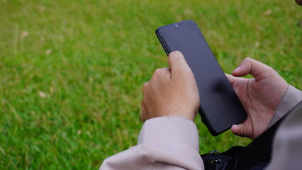 A close-up photo of a hand playing with a cell phone on a large stretch of grass creates a contrast between modern technology and the outdoors.