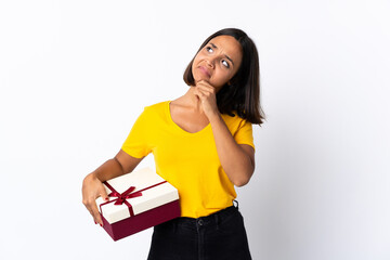 Young latin woman holding a gift isolated on white background and looking up