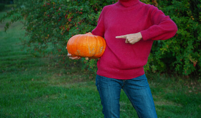 Woman holding big orange pumpkin and showing by finger on it. Autumn Halloween concept
