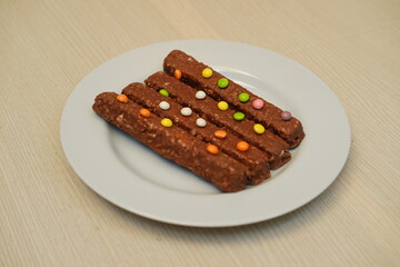 Chocolate bars on a white plate with colorful candies in the background