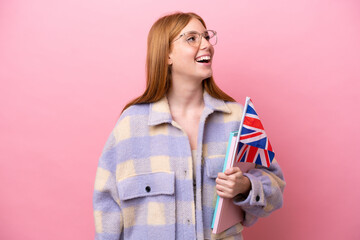 Young redhead woman holding an United Kingdom flag isolated on pink background laughing