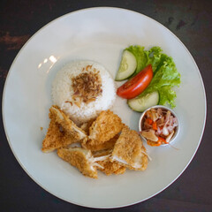 Rice with breaded chicken, vegetable and sambal matah on a white plate