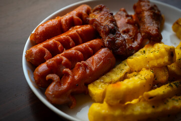 mixed sausage, french fries, and chicken wings cafe platter. Served on white plate, over wooden table surface, in cafe environment