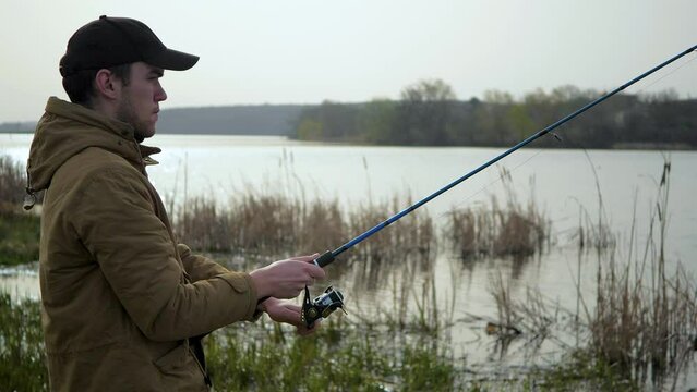 A young man is fishing on the river. Against the background of the blue sky, in nature, the fisherman watches the fish pecking and receives the pleasure of communicating with nature.
