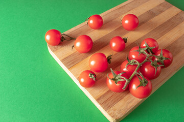 Cherry tomatoes on wooden board on green background. Copy space