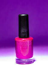 A close-up of a nail polish bottle filled with bright yellow nail polish. The bottle has a cylindrical shape with a black lid and stands against a dark purple background.