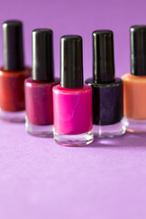 A collection of nail polish bottles are presented against a purple background. In the foreground is a black nail polish bottle with black glitter, while in the background are bottles.
