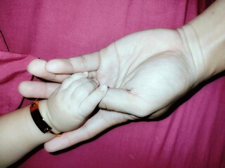 Baby girl's hand with gold bracelet holding her father's hand