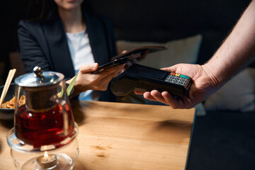 Woman pressing smartphone to the pos-terminal the waiter holding