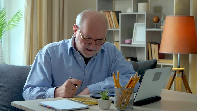 An elderly, gray-haired businessman, wearing a blue shirt, is working on a financial report on a computer. He is very annoyed due to the inaccuracy of the data. Remote work from home.