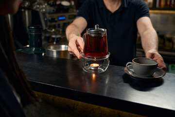 Bartender preparing one cup with saucer and teapot with freshly brewed tea